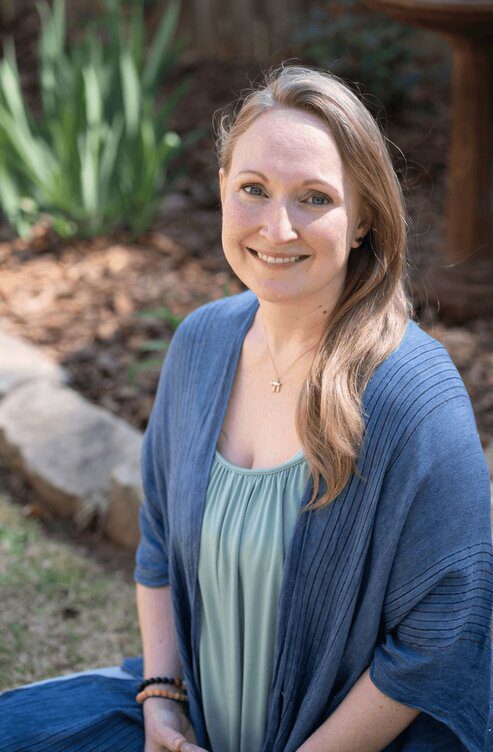 Meditation teacher and podcast host Meryl Arnett smiling wearing a blue cardigan sitting out in nature with plants in the background