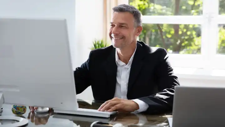 Older man in blazer sits in front of his computer trying to find the right contact person.
