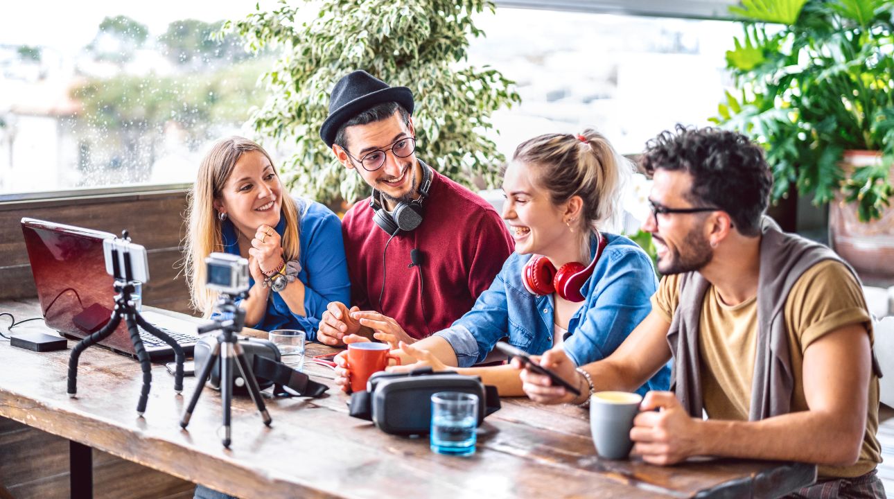 group of young people sitting at outside table with cameras taking video for email marketing campaigns