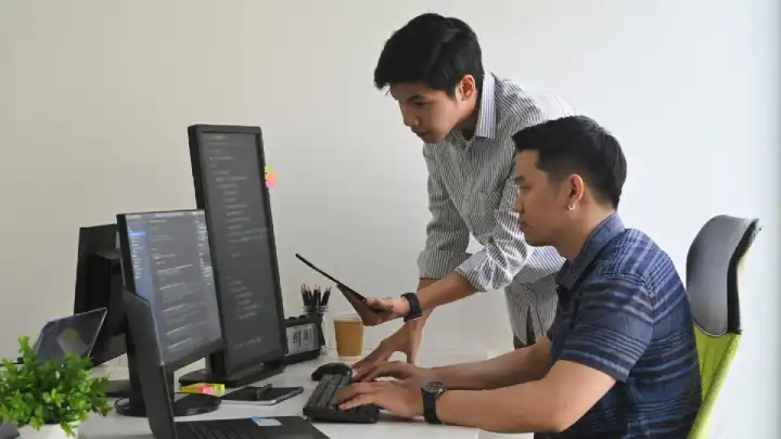 Two young men, one with an earring, sit in front of hte computer while avoiding the cost of not email validating emails.