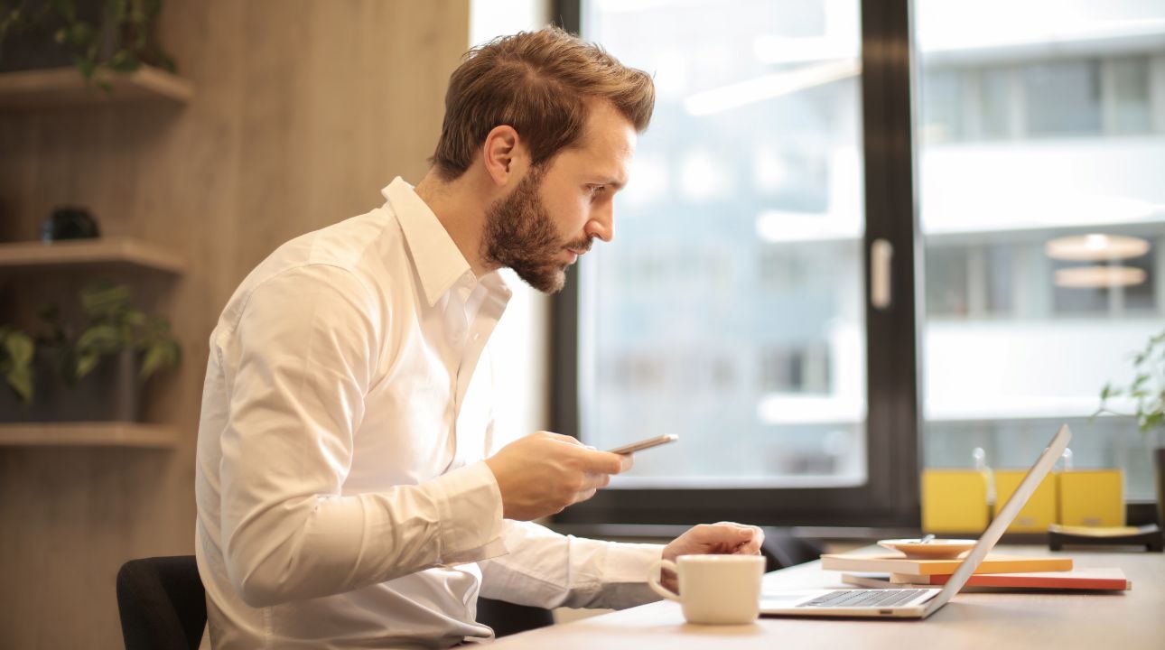 Man working on his phone and laptop learning about email bounce reduction for protecting business revenue