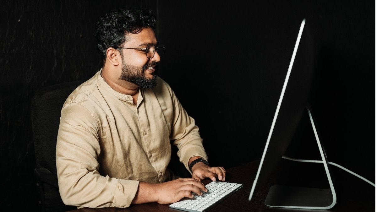 Bespectacled South Asian man sits at computer to use email validation.