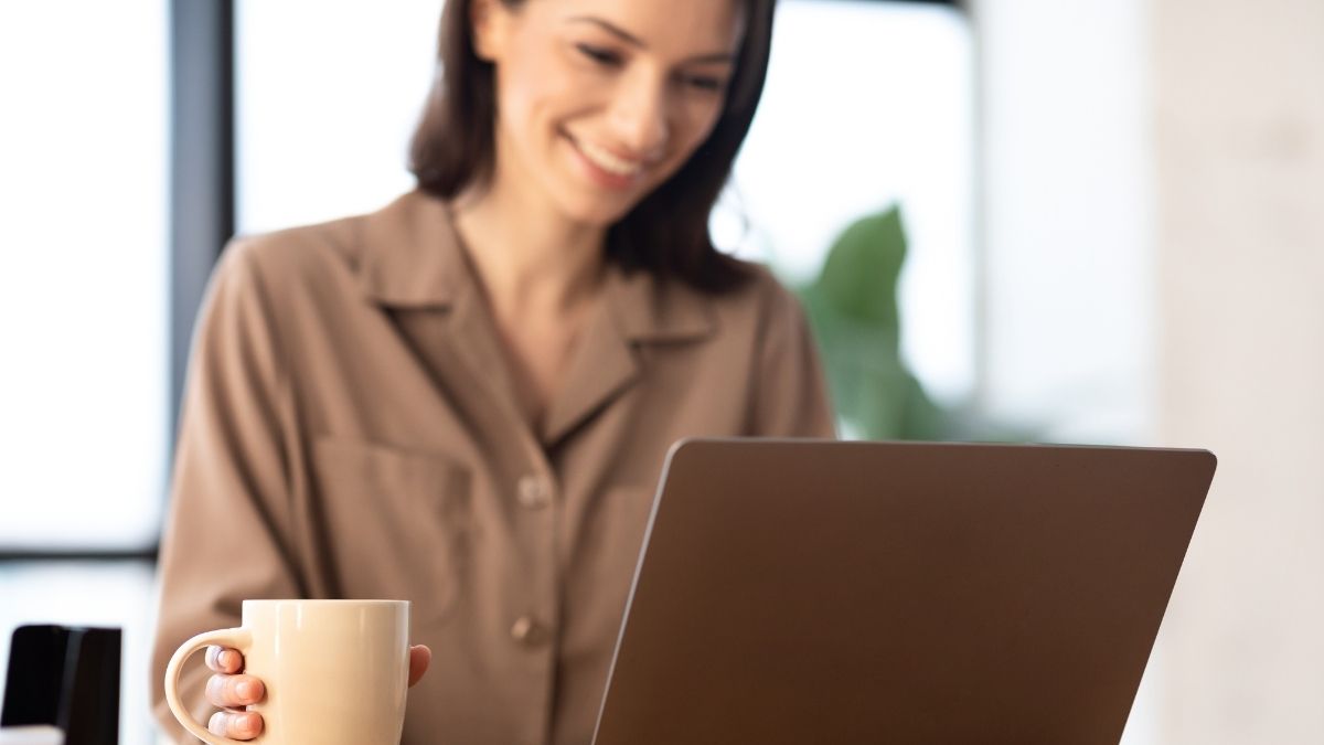 Woman with brown hair sits in front of laptop, completely content with her sender reputation. Coffee mug is nearby.