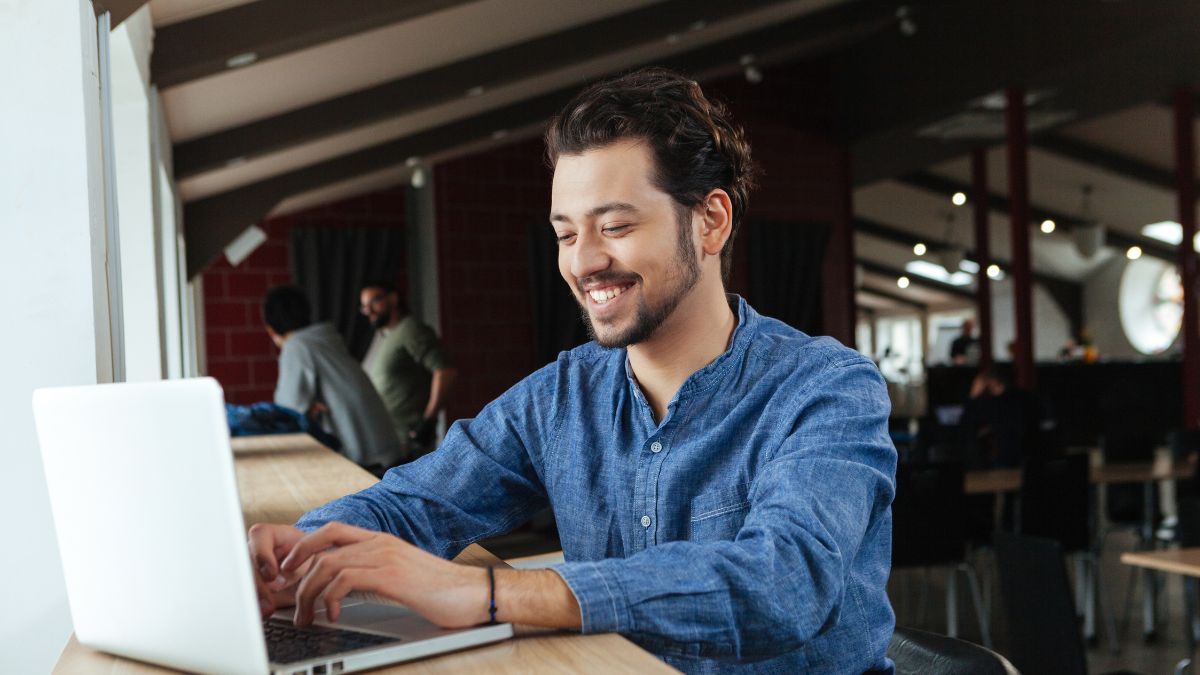 Bearded young man in denim shirt sits at his laptop trying to write an authentic email instead of using AI.