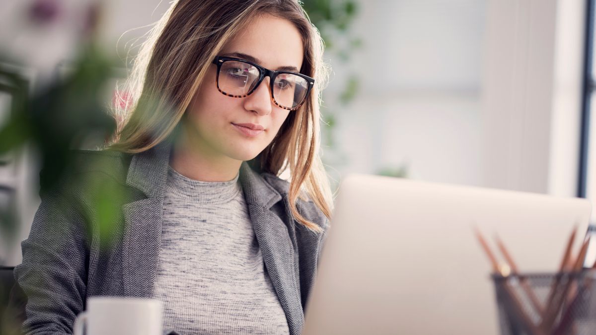 Young bespectacled woman sits in front of her laptop to set up email automation using her newly cleaned list.