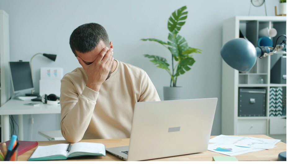 Young man puts his hand on his face in anguish due to email fatigue.