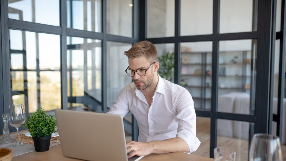Photo of bespectacled professional young man seated in front of a laptop learning about catch-all email configurations.